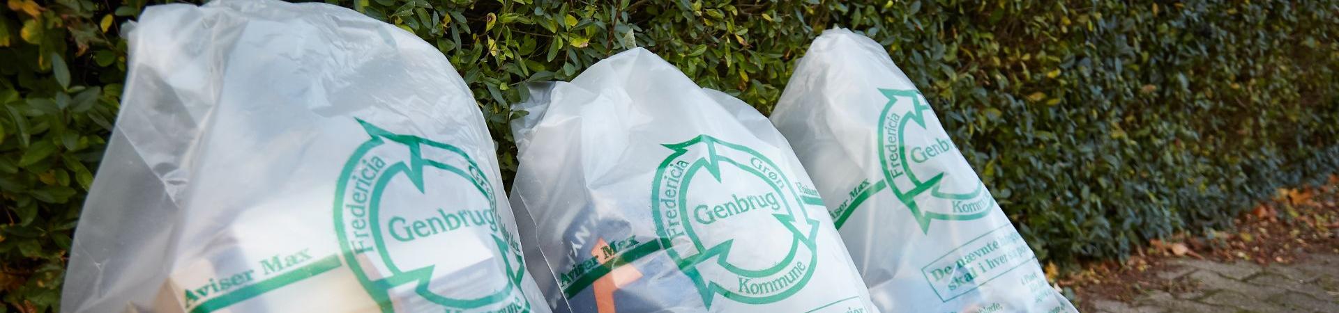 Tre klare sække med genbrugsmaterialer i som står foran en grøn hæk